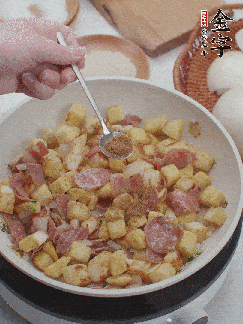 起鍋少油，煸香洋蔥丁、蔥白，加入金字培根火腿翻炒幾下，再加入饅頭丁、1小勺孜然粉、少許鹽翻炒均勻并鋪平。